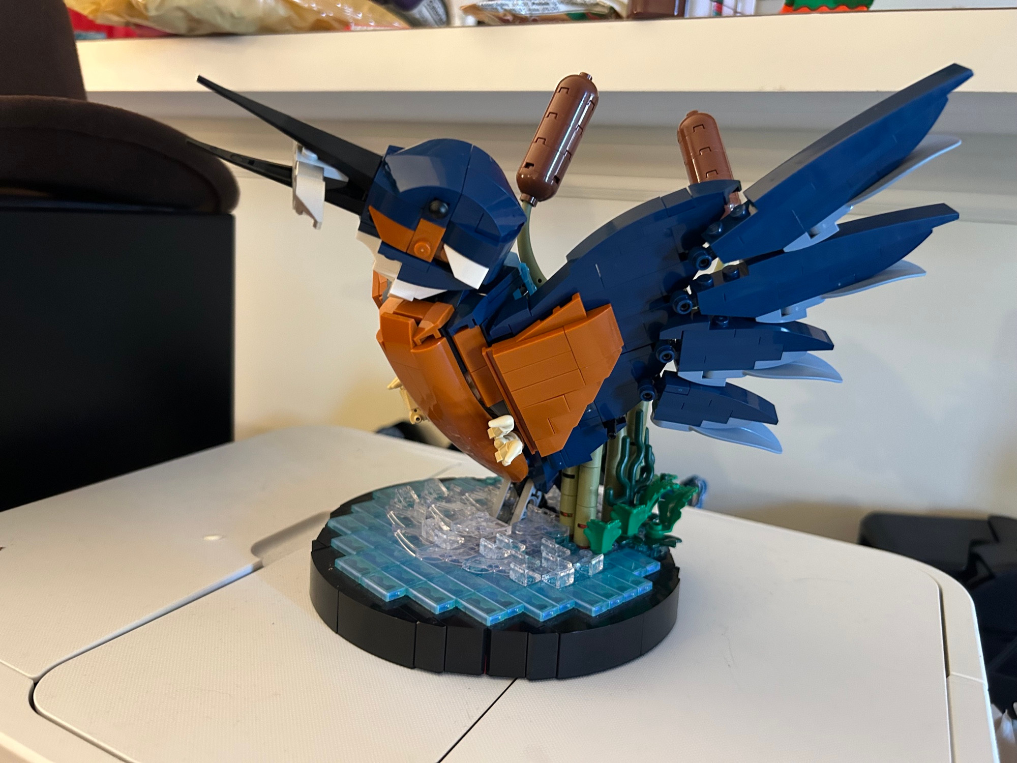 Image of the LEGO Kingfisher set. It is sitting atop a white printer. The kingfisher is in an action pose with its wings outstretched and a fish in its mouth.